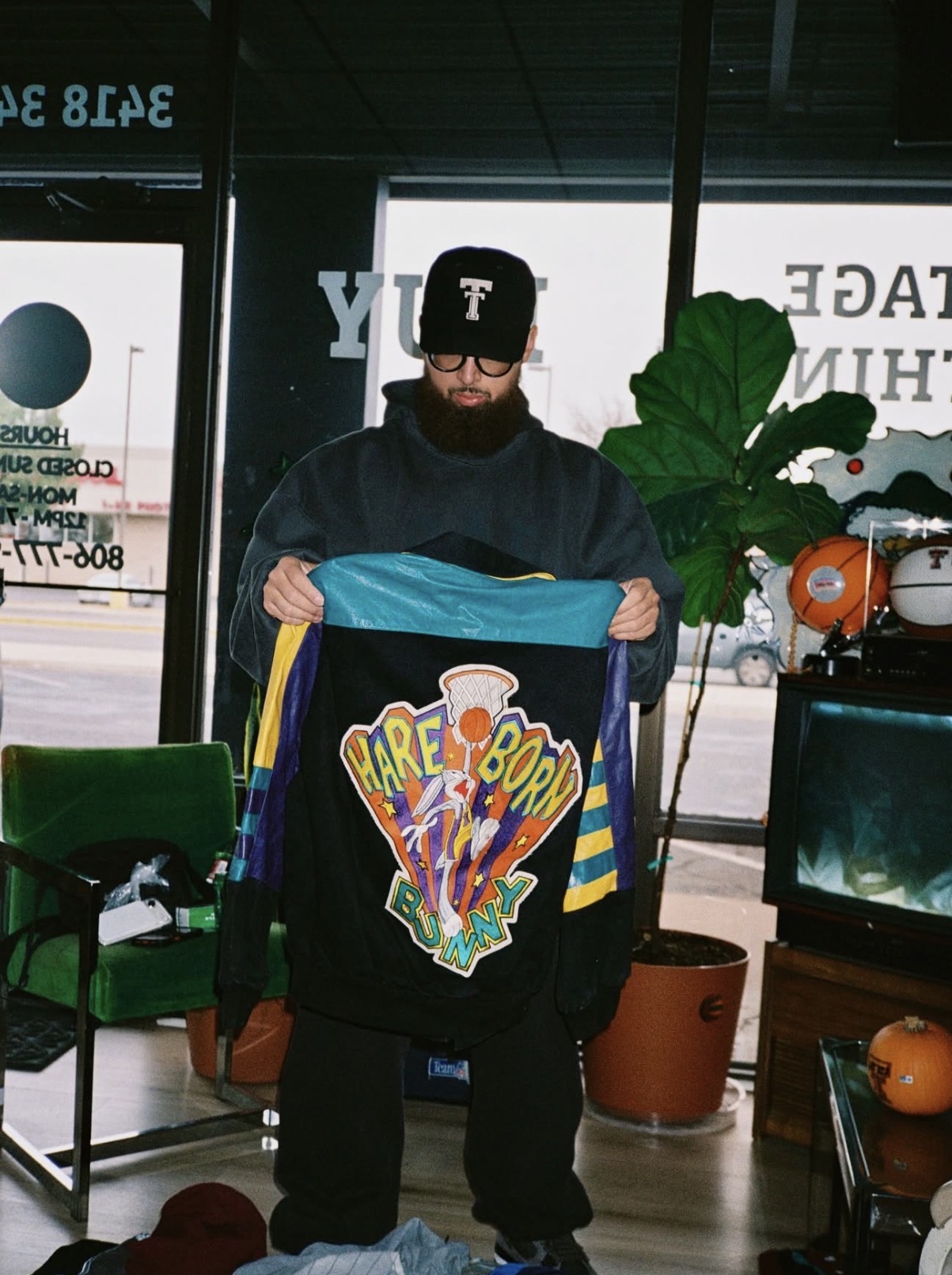 Izrael, owner of Izzy Money Vintage, holding a vintage Space Jam jacket